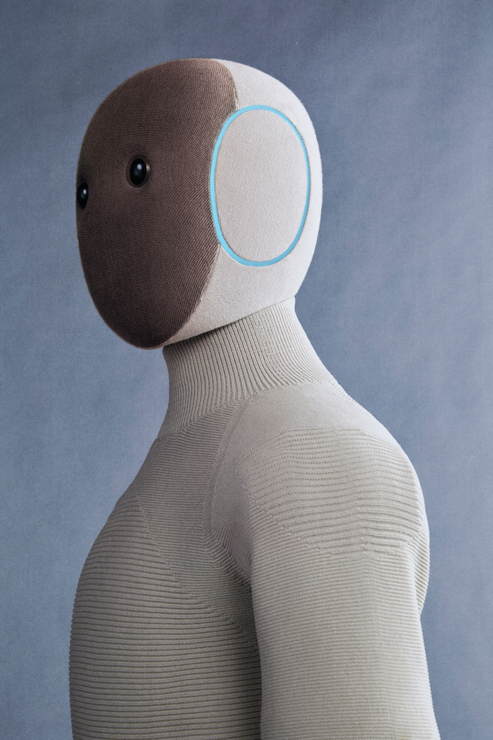 1X NEO home humanoid in a tan knit suit, studio profile of the head, ear ring, and torso